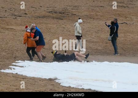 West Bay, Dorset, UK. 20th Oct, 2021. UK Weather. A Walker on the beach falls over as he runs from the wash from a large wave crashing ashore at West Bay in Dorset on a day of heavy showers and gusty winds. Picture Credit: Graham Hunt/Alamy Live News Stock Photo