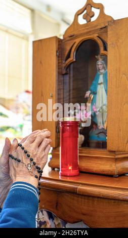 hands in a position of supplication towards a wooden niche containing a saint with a lit candle Stock Photo