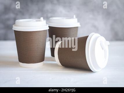 Three brown disposable paper coffee cup with white caps on wooden table. Takeaway drink and eco-friendly tableware concept Stock Photo