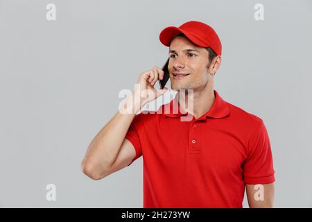 Young delivery man wearing uniform smiling while talking on cellphone isolated over white wall Stock Photo