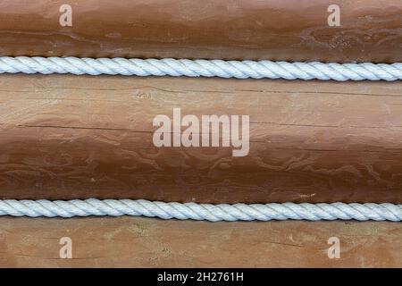Wall of brown painted logs decorated with white braided ropes for use as abstract backgrounds and textures. Stock Photo