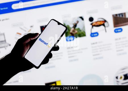 Walmart is an American multinational retail corporation. A smartphone with the Walmart logo in a hand on background of website catalog. Stock Photo