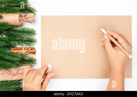 top view of woman hands writing New Year wish list on craft paper with frame made of Christmas tree branches and gift boxes Stock Photo