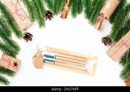 set of gift-wrapped craft pens in frame of Christmas tree branches and cinnamon bundles on white insulated background Stock Photo
