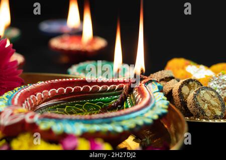Detailed Closeup Of Big Colorful Clay Diya Deep Or Dia Oil Lamps In Decorated Brass Thali Glowing In Dark. Theme For Diwali Pooja, Navratri, Happy New Stock Photo