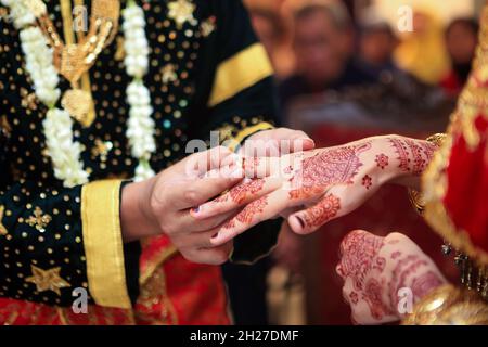 Young Asian muslim couple holding hand and putting wedding ring each other in a traditional Minangkabau culture ceremony.