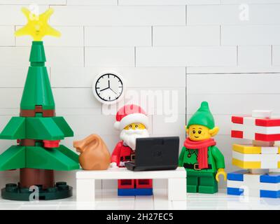 Tambov, Russian Federation - October 17, 2021 Lego Santa Claus minifigure in his office working on his laptop with an elf standing near him. Close up. Stock Photo