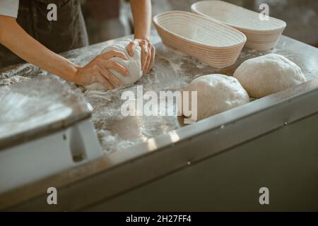 Worker kneads dough making bread at metal table in modern craft bakery shop Stock Photo