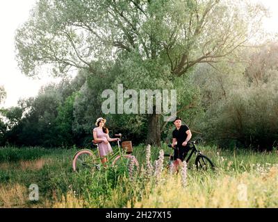 Man and woman resting on bicycles at summer nature. Coutryside or park with greenery. Young couple enjoing on bicycles. Stock Photo