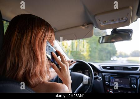 Over the shoulder view of a young woman talking on her mobile phone while driving. Stock Photo