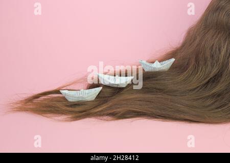 Closeup shot of a woman hair with three white paper boats on a pink background Stock Photo