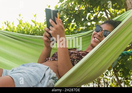 Beautiful dark-skinned woman reads in a hammock by the ocean Stock Photo