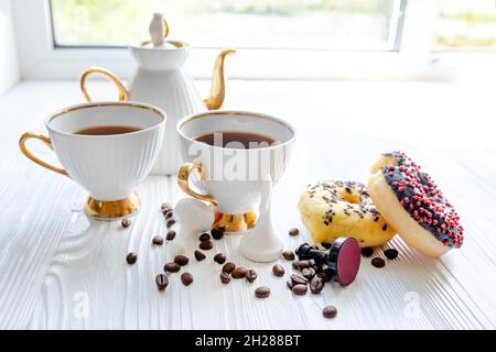 White and black chess pieces on white windowsill. Morning coffee of a couple in love with sweet donuts and a game of chess. White cups and a vintage t Stock Photo