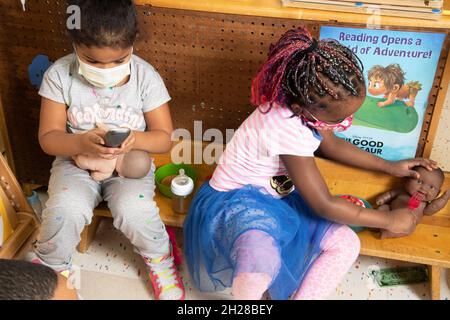 Education Preschool 4-5 year olds two girls pretend play, one feeding doll, the other making phone call or texting with doll on her lap, both wearing Stock Photo