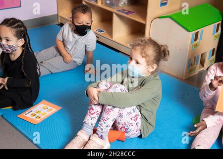Education Preschool 3-4 year olds morning meeting small gropu of children listening, all wearing face masks to protect against Covid-19 infection Stock Photo