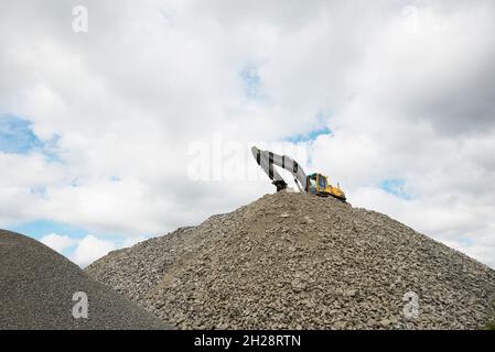 Excavator on top of a pile of gravel and stones Stock Photo