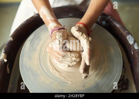 Above view of unrecognizable woman with dirty hands shaping clay while working on pottery wheel Stock Photo