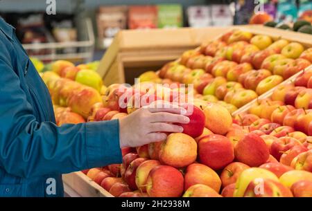 Choosing organic apple in the market. Woman selecting fresh red apples in grocery store. Female hand taking fruit from a shelf. Street view, travel Stock Photo