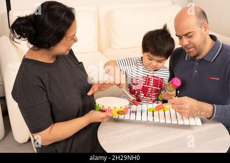 2 year old toddler boy playing wooden xylophone with a mallet, mother and father making music with hiim using tambourine and another mallet Stock Photo
