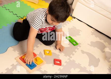 Two year old toddler boy playing with shape sorter puzzle, matching clolors Stock Photo