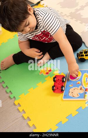 2 year old toddler boy at home turning puzzle piece to fit into space rotating wrist Stock Photo