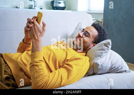 Young African Lying on the Couch Using a Smartphone Stock Photo
