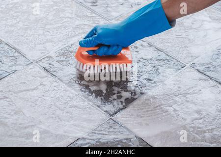 Hand of man wearing blue rubber gloves is used to convert scrub cleaning on the tile floor. Stock Photo