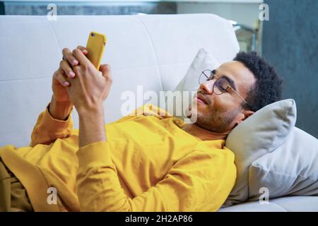 Young African Lying on the Couch Using a Smartphone Stock Photo