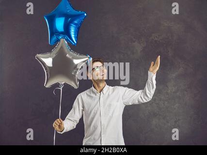Happy smiling young man holding a pair of shiny air balloons for a birthday party Stock Photo