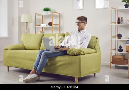 Happy young remote employee working on his laptop while sitting on couch at home Stock Photo