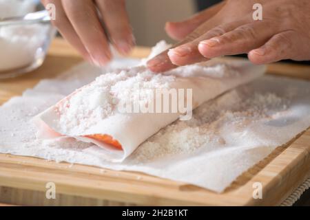 Marinated Salmon with Salt on paper tissue food grade on Wooden cutting plate by Professional hand Chef. Stock Photo