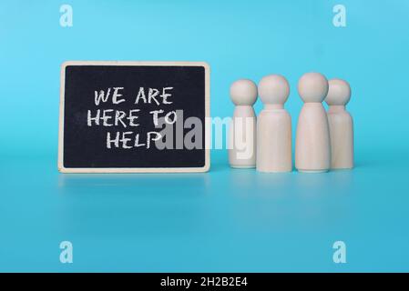 Help, assist and support concept. Wooden dolls with text WE ARE HERE TO HELP on blue background. Stock Photo