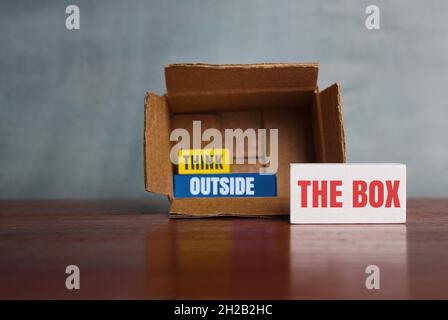 Think differently, unconventionally, or a new perspective concept. Box and wooden cube with text THINK OUTSIDE THE BOX Stock Photo