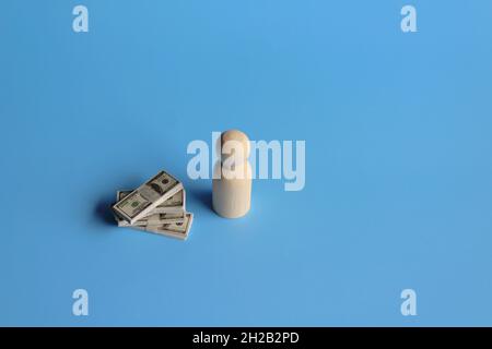 Business and finance concept. Wooden doll with a pile of money on blue background. Copy space for text. Stock Photo