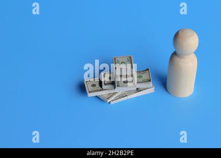 Business and finance concept. Wooden doll with a pile of money on blue background. Copy space for text. Stock Photo