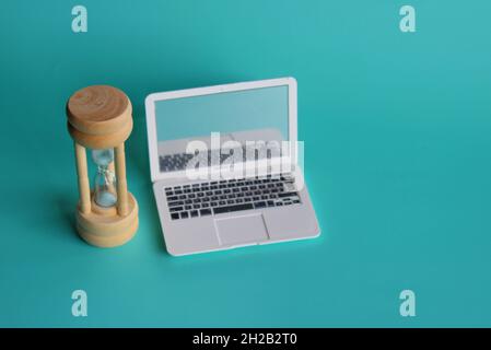 Selective focus image of hourglass and laptop on green background. Screen time limits concept. Stock Photo