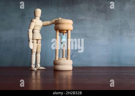 Time management, waiting time concept. Wooden human figure look at the sandglass. copy space for text. Stock Photo