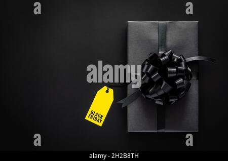 A black gift box with ribbon and yellow price tag puts on black background. Black friday concept. Stock Photo