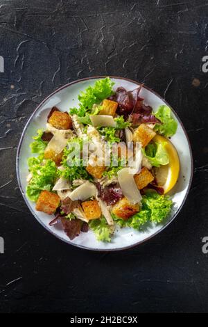 Caesar salad, shot from the top on a black background. Lettuce leaves, crispy croutons and chicken meat, with copy space Stock Photo