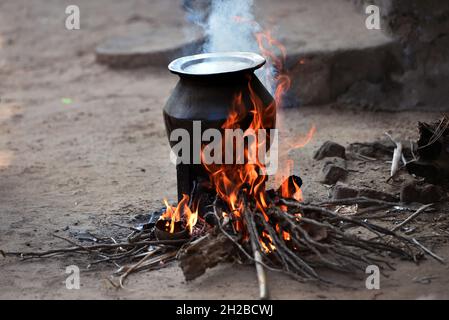 Open fire cooking in an Indian village An aluminum utensil on a temporarily made fire oven. Rural kitchen using bio wood fuel for cooking. Desi Chulha Stock Photo
