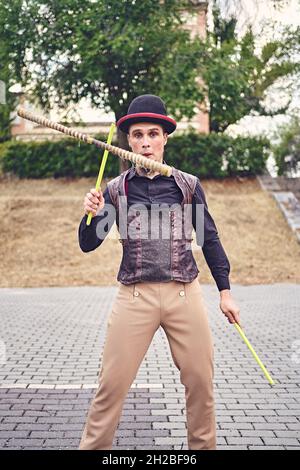 Male performer in fancy suit juggling devil sticks on summer day in park Stock Photo