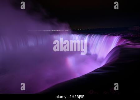 Niagara Falls illuminated in purple light with rainbows from the mist, Canada. Stock Photo
