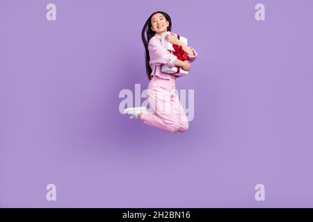 Full size profile photo of sweet millennial brunette lady jump hug present wear jacket jeans sneakers isolated on violet background Stock Photo