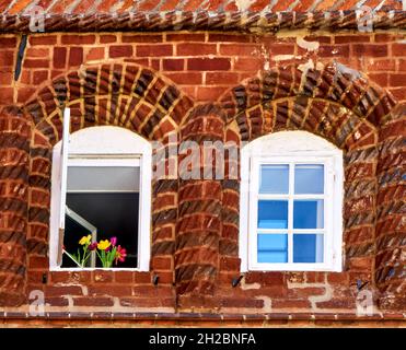 Window in an old house wall made of red bricks with an arrangement of colorful tulips in the left window and blue light in the right one Stock Photo