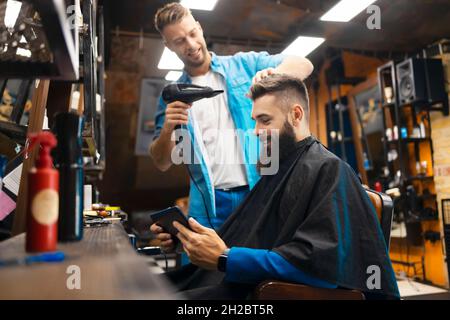Young bearded man using a smartphone at the hairstylist Stock Photo