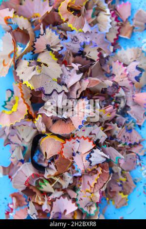 Wooden pencil shavings and colorful crumbs of graphite from sharpener on soft blue pastel paper background. Top view. Design elements for poster, bann Stock Photo