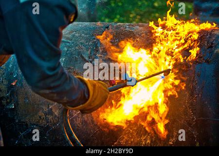 The texture of hot metal from acetylene welding. Welder's hands in protective gloves during operation. Cutting a metal pipe outside during the day. Stock Photo