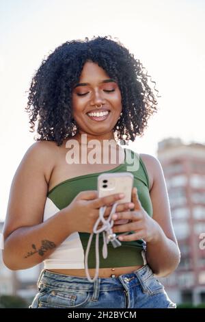Young latina with curly hair sending a message with a mobile phone Stock Photo