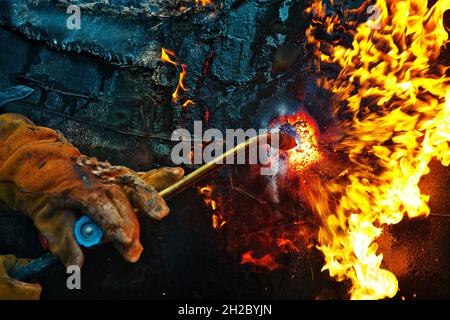 The texture of hot metal from acetylene welding. Welder's hands in protective gloves during operation. Cutting a metal pipe outside during the day. Stock Photo