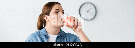 Plus size woman drinking fruit smoothie in kitchen, banner Stock Photo